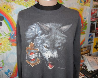 May include: A gray long-sleeve sweatshirt with a wolf graphic and the Harley Davidson Motor Co. logo. The wolf is snarling with its mouth open and teeth showing. The logo is in a red circle with the words "Harley Davidson Motor Co." around it.