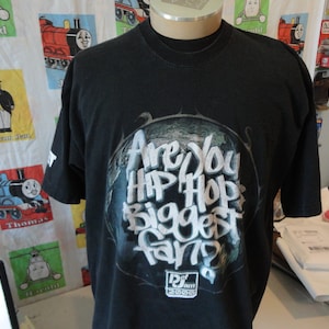 May include: Black t-shirt with a white graphic print of a globe with the text "Are You Hip Hop Biggest Fan?" and the text "DJ Jam 2005" below the globe.