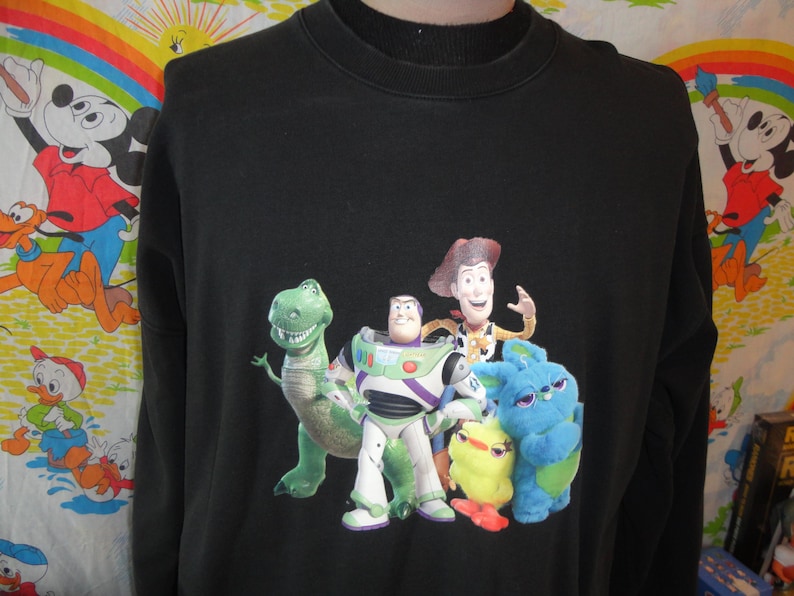 Może przedstawiać: Czarna bluza z długim rękawem z nadrukiem postaci z serii Toy Story. Postacie to Woody, Buzz Astral, Rex i fioletowy kosmita.