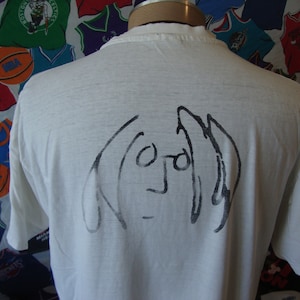May include: White t-shirt with a black and white line drawing of John Lennon on the back.