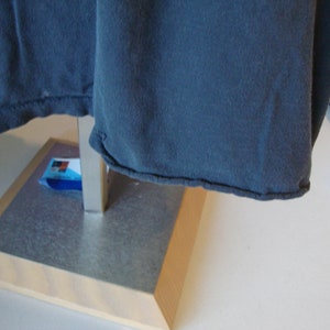 May include: A dark blue t-shirt with a folded hem, hanging on a metal stand with a wooden base.