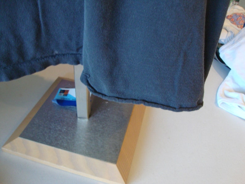 May include: A dark blue t-shirt with a folded hem, hanging on a metal stand with a wooden base.