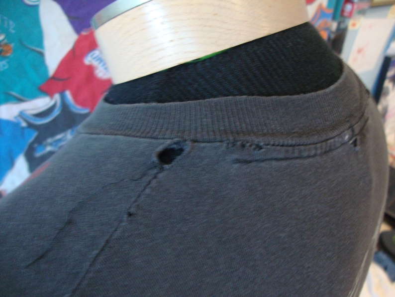 May include: A black t-shirt with a small hole near the neckline. The shirt is on a mannequin.