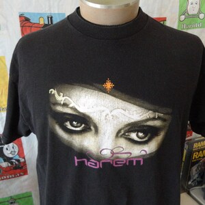 Könnte beinhalten: Schwarzes T-Shirt mit einem Aufdruck eines Frauenauges mit einem Juwelenband und dem Wort "Harem" in Lila.