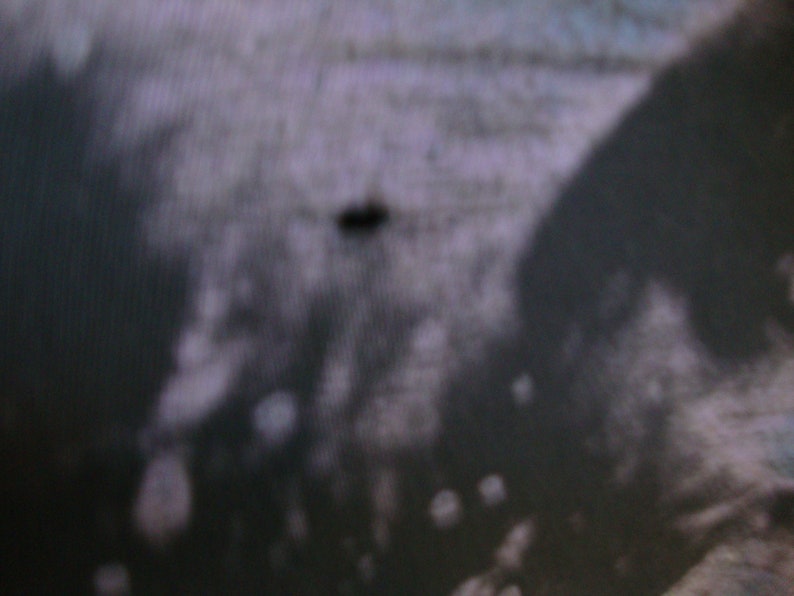 Puede incluir: Primer plano de una tela texturizada gris oscuro con una peque&ntilde;a mancha negra en el centro.