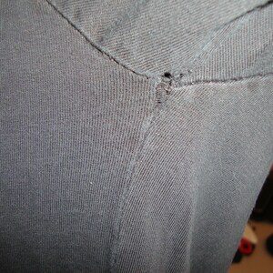 Puede incluir: Primer plano de una camiseta negra con un peque&ntilde;o agujero en la costura del hombro.