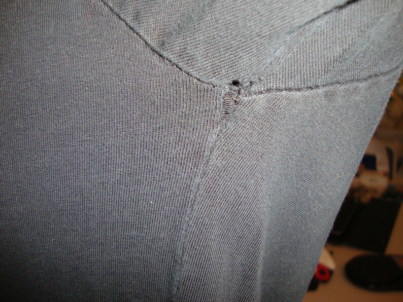 Puede incluir: Primer plano de una camiseta negra con un peque&ntilde;o agujero en la costura del hombro.