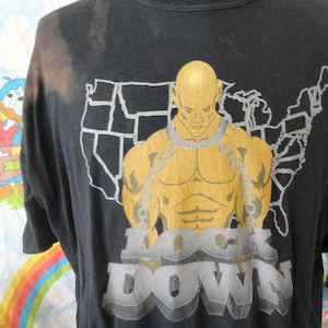 May include: Black t-shirt with a graphic of a muscular man in chains, standing in front of an outline of the United States. The text "LOCK DOWN" is printed below the image.