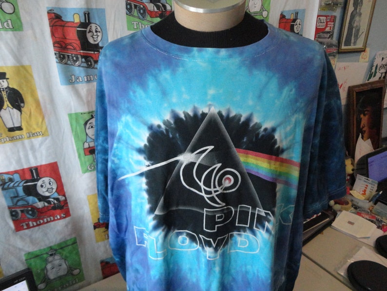 May include: A blue tie-dye t-shirt with a black and white graphic of Pink Floyd's Dark Side of the Moon album cover.