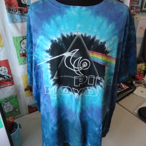 May include: A blue tie-dye t-shirt with a black and white graphic of Pink Floyd's Dark Side of the Moon album cover.