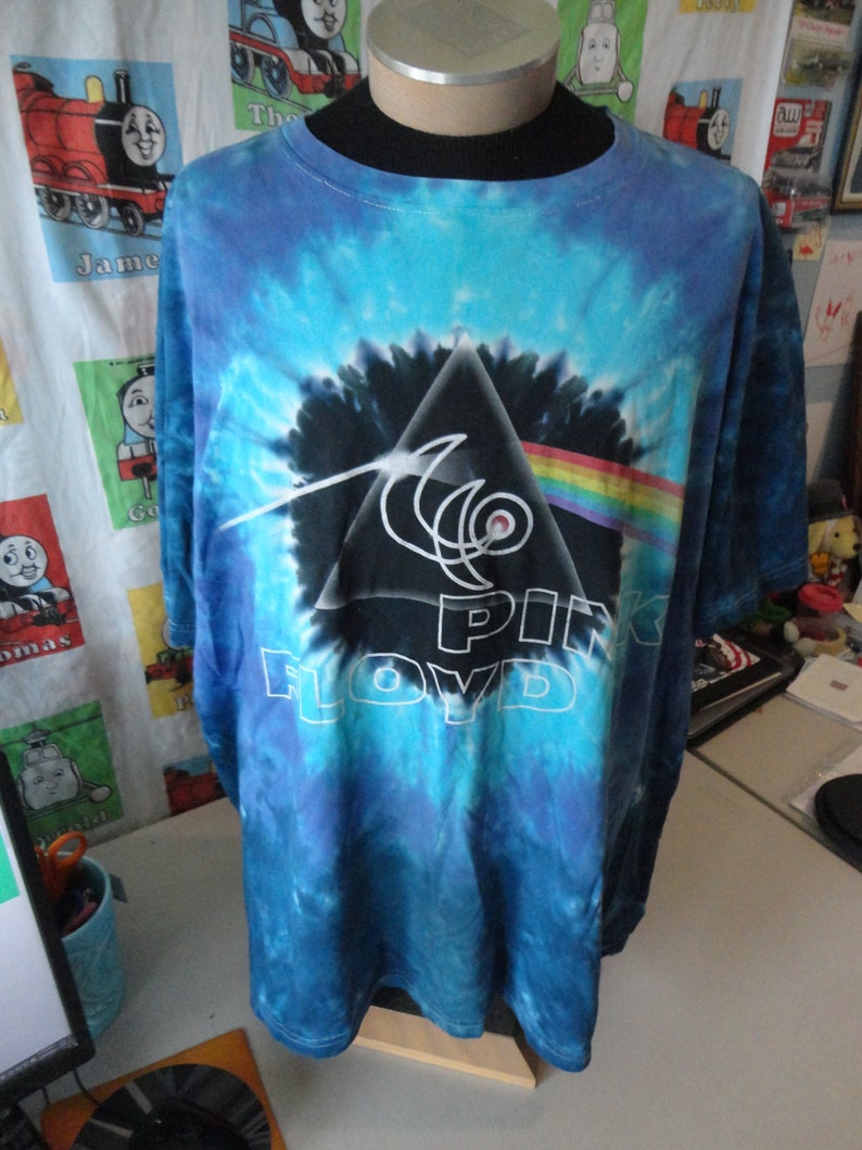 May include: A blue tie-dye t-shirt with a black and white graphic of Pink Floyd's Dark Side of the Moon album cover.