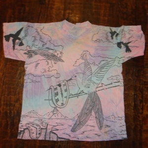May include: A tie-dye t-shirt with a hummingbird, clock, and birds in flight design. The shirt is pink, blue, and purple.
