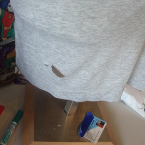 Peut inclure: Un t-shirt gris avec un petit trou dans le tissu.