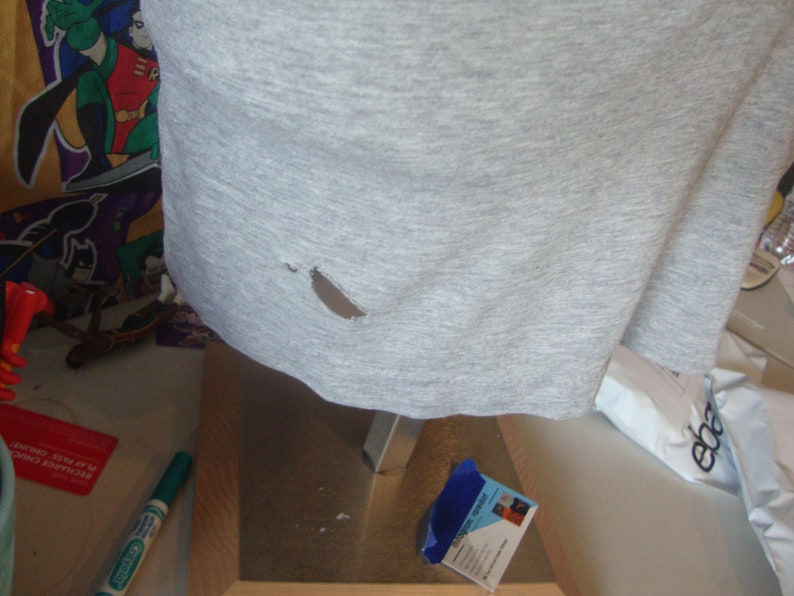 Peut inclure: Un t-shirt gris avec un petit trou dans le tissu.