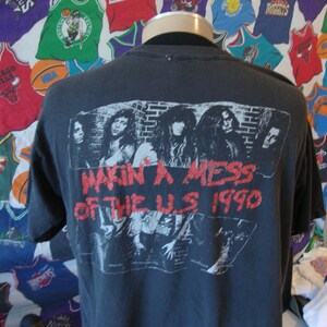 May include: Black t-shirt with a band graphic on the back. The graphic features a band of four people with the text "Makin' a Mess of the U.S. 1990".