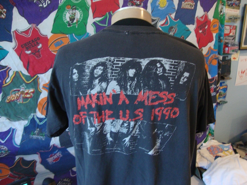 May include: Black t-shirt with a band graphic on the back. The graphic features a band of four people with the text "Makin' a Mess of the U.S. 1990".