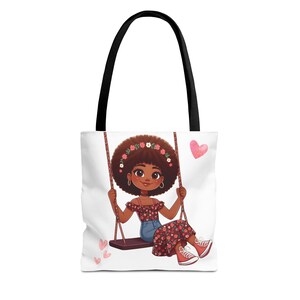 Può includere: Borsa tote bianca con manico nero con un'illustrazione di un cartone animato di una ragazza su un'altalena. La ragazza ha la pelle scura, una fascia floreale e indossa un top floreale, pantaloncini di jeans e scarpe da ginnastica rosse. Cuori rosa sparsi.