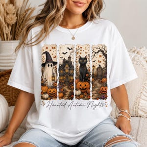 Pode incluir: Uma t-shirt branca com uma estampa gráfica de quatro painéis verticais retratando um fantasma com chapéu de bruxa, uma casa assombrada, um gato preto sobre uma abóbora e um cemitério. O texto "Haunted Autumn Nights" está impresso em preto.