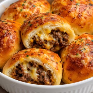 Può includere: Un gruppo di panini dorati al forno, farciti con carne macinata condita e formaggio giallo fuso. I panini presentano una crosta lucida e tostata con piccole erbe verdi, e due panini sono tagliati a metà per rivelare il ripieno saporito.