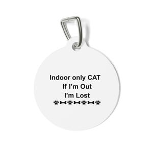 Puede incluir: Una placa de identificación blanca y redonda para mascotas con un lazo de metal plateado. La placa tiene el texto "Indoor only CAT If I'm Out I'm Lost" en negro, junto con huellas de patas y huesos.