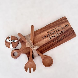 May include: A wooden serving board with a handle, two wooden spoons, and a round box tied with a ribbon. The board has the text "Let all that you do be done in love." and the names "BRITTANY & CHRIS 07.06.15".