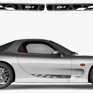 Puede incluir: Coche deportivo plateado con detalles en negro y franjas de carreras. El coche tiene un diseño elegante con un alerón y llantas personalizadas. Las franjas de carreras incluyen un diseño de bandera a cuadros y el texto "RX-7".