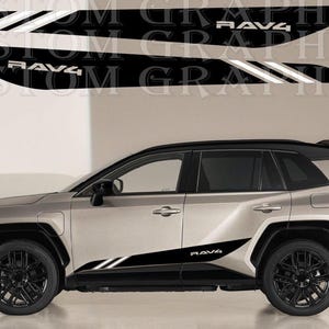 Könnte beinhalten: Ein Set aus zwei schwarz-weißen Vinyl-Seitenaufklebern für ein Fahrzeug, mit einem spitz zulaufenden Design, zwei parallelen Streifen und dem Schriftzug RAV4. Die Aufkleber sind an der unteren Seitenverkleidung eines silbernen SUVs angebracht.