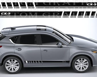 May include: A silver SUV shown in profile view featuring a black and orange racing-style side decal with the text CX-5. The decal consists of a long horizontal stripe with a series of vertical rectangular segments and a single orange accent block.