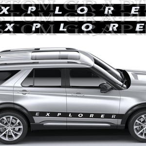 Op de afbeelding: Een zilveren SUV met zwarte afwerking en het woord "EXPLORER" in witte letters op de zijkant. De afbeelding toont ook de tekst "CUSTOM GRAPHICS" in wit op een zwarte achtergrond.