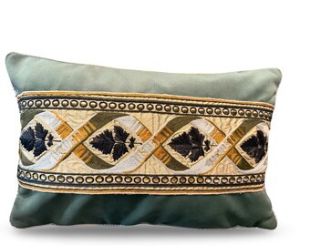May include: A rectangular decorative pillow in shades of green, with an embroidered band across the center. The band features a repeating pattern of black leaves, gold, and white accents, and is bordered by gold beads.