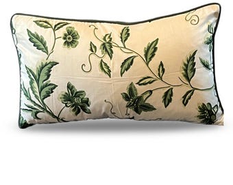 May include: Rectangular decorative pillow with a cream-colored background and a green floral pattern. The design features stylized green leaves and flowers with a dark green border. The pillow is a home decor item.