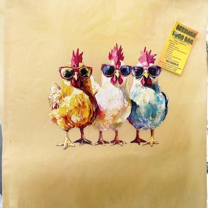 May include: A beige reusable food bag featuring a watercolor illustration of three chickens wearing sunglasses. The chickens are in shades of yellow, white, and blue. A yellow tag with text is attached to the bag.