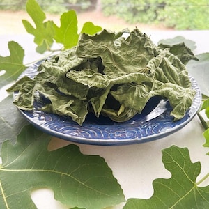 Puede incluir: Un plato de cerámica azul con un montón de hojas verdes secas. El plato está rodeado de hojas verdes.