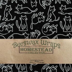 May include: Black beeswax wraps with a white cat pattern. The wraps are from the Homestead Collective. The text "Beeswax Wraps" and "Homestead Collective" are printed on the packaging.