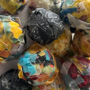 May include: A collection of colorful, fabric-covered spheres. The spheres are made from various patterned fabrics in shades of yellow, blue, red, and black. The fabric is layered and textured, creating a unique, handcrafted appearance.