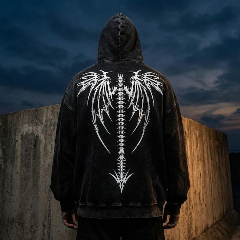 May include: A black hooded sweatshirt featuring a white, stylized spine and wing design on the back. The design is detailed and graphic, with a distressed, vintage appearance. The hoodie has a drawstring and a front pocket.
