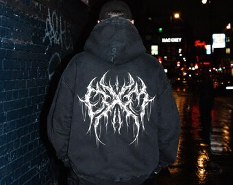 May include: A black hooded sweatshirt featuring a large, white, intricate, symmetrical graphic print on the back. The design consists of sharp, elongated, and jagged lines that form a complex, abstract pattern across the center of the back.