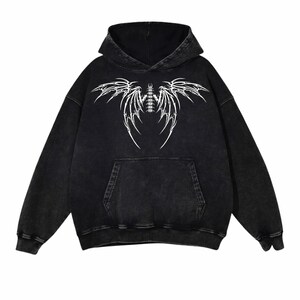 May include: Black hoodie with a white graphic design. The design is a stylized wing or insect-like pattern. The hoodie has a hood and a front pocket. It is made of a soft, comfortable material.