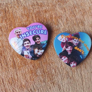 Könnte beinhalten: Zwei herzförmige Ansteckbuttons mit Fotos einer Boyband. Der linke Button hat einen violetten Hintergrund mit dem Text "YOU'RE INSECURE". Der rechte Button hat einen blauen Hintergrund mit dem Text "if you ever feel alone don't."