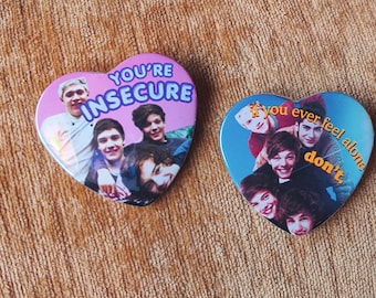 May include: Two heart-shaped pin-back buttons featuring photographs of a boy band. The left button has a purple background with the text "YOU'RE INSECURE". The right button has a blue background with the text "if you ever feel alone don't."