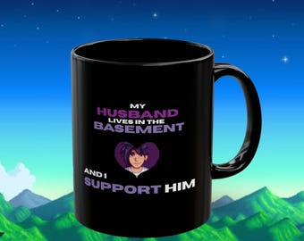 May include: Black ceramic mug with the text "MY HUSBAND LIVES IN THE BASEMENT AND I SUPPORT HIM". The mug features a pixelated image of a woman inside a purple heart. The mug has a black handle and a glossy finish.