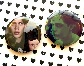 May include: Two round pinback buttons. One button features a young man with a doll, the other a green-toned portrait of a person. The background is white with black heart shapes.
