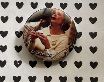 Könnte beinhalten: Ein runder Button mit dem Bild einer Frau, die ein Gebäck hält, mit dem Text "Good for her". Der Button befindet sich vor einem weißen Hintergrund mit einem Muster aus schwarzen Herzen.