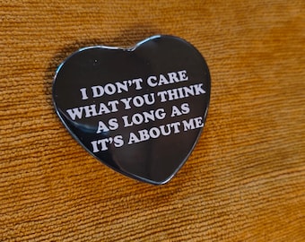 May include: A heart-shaped black pin with white text that reads, I DON'T CARE WHAT YOU THINK AS LONG AS IT'S ABOUT ME. The pin has a smooth, glossy finish and a classic heart silhouette, featuring bold, capitalized lettering centered on the surface.