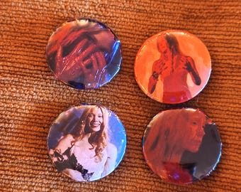 May include: Four circular pinback buttons featuring photographic imagery. The top left button shows a person with hands over their face in red tones. The top right button depicts a person in orange. The bottom left shows a smiling person in white. The bottom right is a dark red profile.
