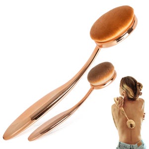 May include: Two rose gold makeup brushes with oval brush heads. The larger brush is angled towards the top left, while the smaller brush is angled towards the bottom right. The brush heads are a light brown color.