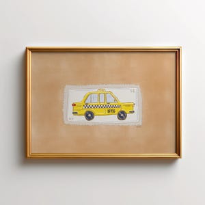 May include: A framed artwork featuring a yellow NYC taxi illustration. The taxi is depicted on a postage stamp-like background with the text "NYC". The artwork is encased in a gold-colored frame, set against a neutral background.