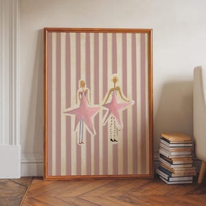 May include: A framed vertical wall art print featuring two stylized figures wearing large pink star-shaped costumes. The background consists of alternating vertical stripes in muted pink and cream colors. The figures have thin limbs and wear patterned leggings.