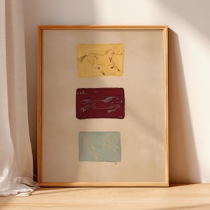 Puede incluir: Una lámina de arte enmarcada que presenta tres bloques rectangulares apilados en amarillo, rojo oscuro y azul claro. Cada bloque contiene una ilustración de líneas simple y dibujada a mano de un caballo en movimiento. El fondo es beige neutro.