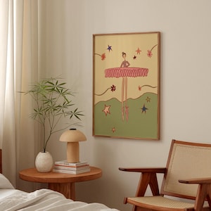 May include: A framed art print featuring a whimsical illustration of a ballerina. The ballerina is depicted with a pink tutu and pointe shoes, set against a backdrop of stars and a green landscape. The artwork is framed in a natural wood tone.